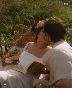 a woman in white dress sitting on grass reading a book next to a picnic table