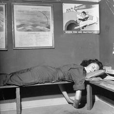 a woman laying on top of a wooden bench next to a wall covered in posters