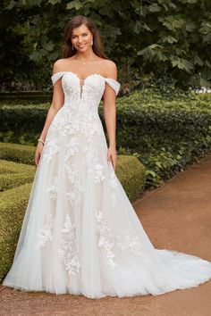 a woman in a white wedding dress standing on a path with bushes and trees behind her