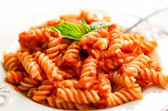 a white plate topped with pasta covered in sauce and garnished with a green leaf