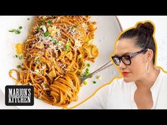 a woman with glasses is looking at a plate of pasta on the table in front of her