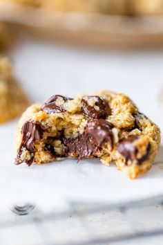 a chocolate chip cookie is half eaten on a white surface with other cookies in the background