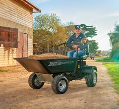 a man riding on the back of a green lawn mower next to a barn