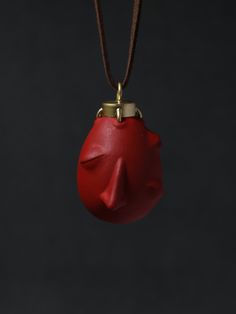 a red object hanging from a cord on a black background in the shape of a face