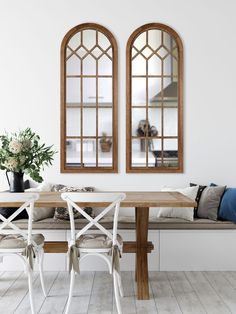 two arched windows above a wooden table with white chairs