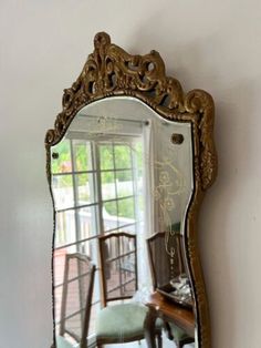 a mirror that is on the wall near a chair and table in front of a window