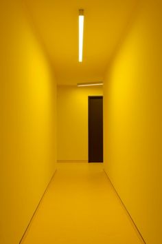 an empty hallway with yellow walls and black door at the end is lit by recess lighting