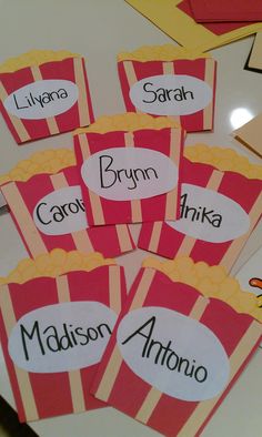 four red and yellow striped popcorn boxes with name tags on them sitting on a table