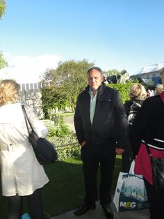 a man in a suit and tie standing next to other people on the grass outside