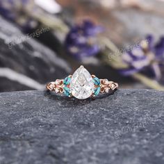 an engagement ring with blue and white stones on top of a stone slab in front of purple flowers