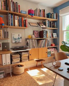 a living room filled with lots of books and furniture next to a window covered in sunlight