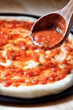 a wooden spoon is being used to dip sauce on a pizza