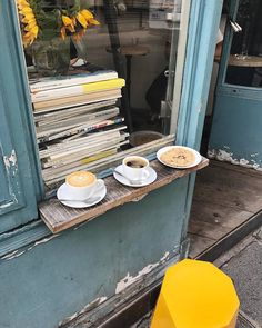 two cups of coffee sit on a window ledge in front of a store with books