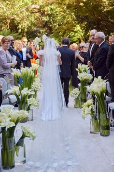 the bride is walking down the aisle with her veil draped over her head and flowers in vases