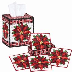 three red poinsettia napkins and two tissue dispensers on a white background