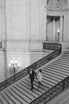 a man and woman are walking down the stairs in an old building with chandeliers