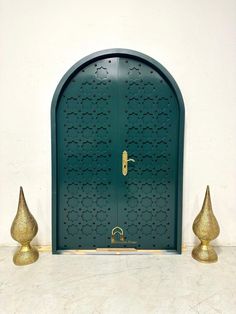 a green door with two gold vases in front of it and a white wall behind it