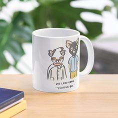 a coffee mug with two dogs on it sitting on a table next to a book