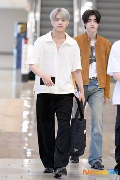 two young men are walking down the street together, one is carrying a black bag