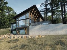 a modern house on top of a hill surrounded by trees and grass in front of a stone wall