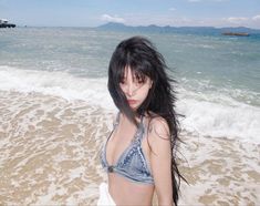 a woman standing on top of a sandy beach next to the ocean with her hair blowing in the wind