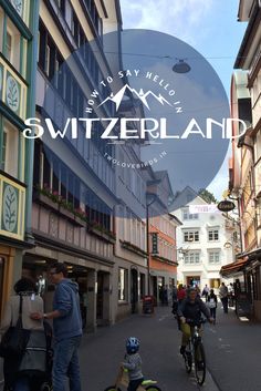 people riding bicycles down a street with buildings in the background and a blue sign that says switzerland