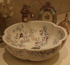 a white bowl with flowers painted on it sitting on a counter next to two mirrors