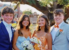 three young people standing next to each other in front of a tree with flowers on it