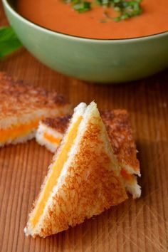 two grilled cheese sandwiches with tomato soup in the bowl behind them on a wooden table