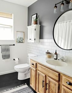 a white toilet sitting next to a bathroom sink under a round mirror in a bathroom