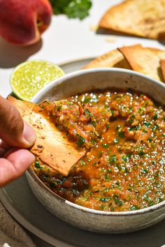 a person dipping salsa into a bowl with tortilla chips and fruit in the background