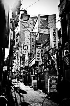 a black and white photo of an alley way with many signs on the side of buildings