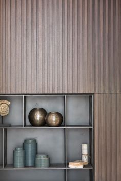 a shelf with vases, books and other items on it in front of a wooden wall