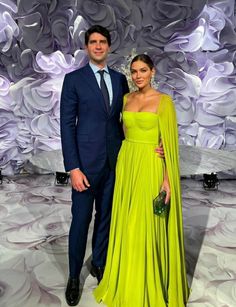 two people standing next to each other in front of a purple wall with flowers on it