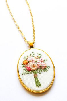 an embroidered necklace with flowers on it is hanging from a gold plated pendant chain