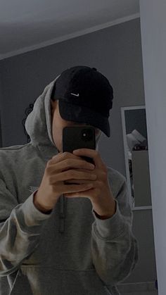 a man taking a selfie in the mirror with his cell phone while wearing a baseball cap