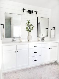 a white bathroom with two sinks, mirrors and plants in vases on the counter