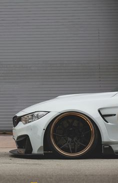 a white car with gold rims parked in front of a garage door on the street