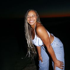 a woman with long braids standing on the beach at night, smiling for the camera