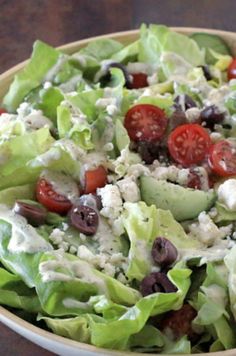 a salad with lettuce, tomatoes and olives in a bowl on a table