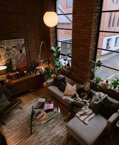 a living room filled with furniture and lots of windows next to a tall brick wall