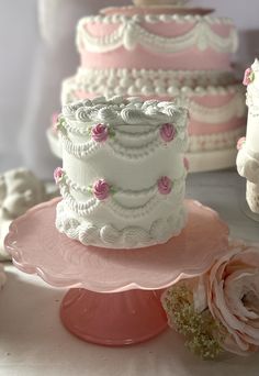 three tiered wedding cake sitting on top of a pink platter next to flowers