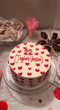 a white cake with red hearts on it sitting on a table next to other desserts