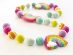 a multicolored felt necklace with balls and clouds on it's end, sitting on a white surface