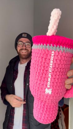 a man holding up a crocheted cup with a toothbrush holder in it