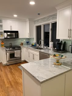 a kitchen with white cabinets and marble counter tops, stainless steel appliances and wooden floors