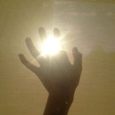 a person's hand reaching out towards the sun