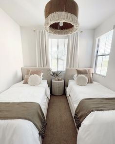 two twin beds in a bedroom with white walls and carpeted flooring, along with a chandelier hanging from the ceiling