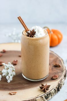 a glass filled with whipped cream and cinnamon on top of a wooden table next to an orange pumpkin