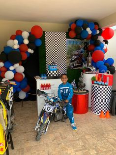 a young boy sitting on a motorcycle in front of a birthday party setup with balloons